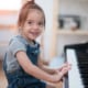A little girl sits at the piano, smiling and ready to play.