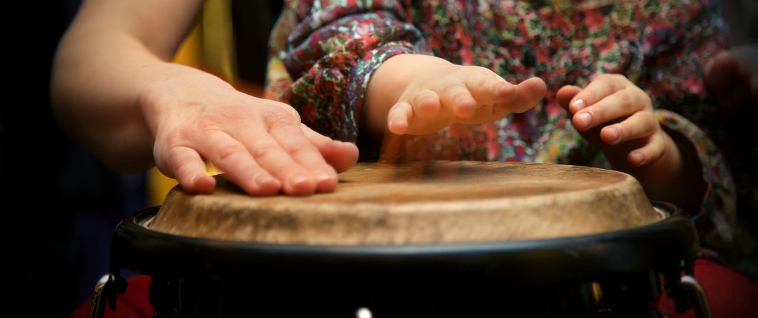 A child and an adult play the drum together.