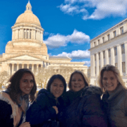 A smiling group of women stands in front of a government building in the winter.